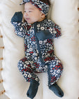 Baby in a floral outfit and headband lying in a crib with white mattress