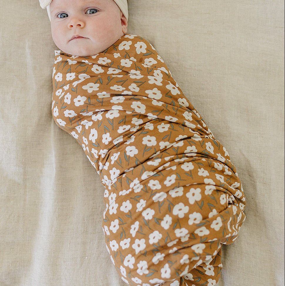 Newborn baby wrapped in a floral swaddle blanket with a headband on a beige background