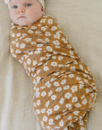 Newborn baby wrapped in a floral swaddle blanket with a headband on a beige background