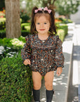 Young girl in a floral dress standing on a sidewalk with greenery in the background