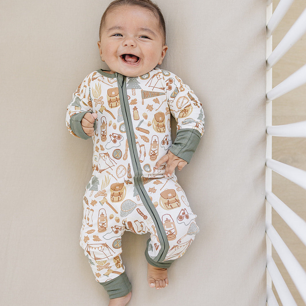 Baby wearing a patterned onesie standing against a neutral wall.
