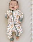 Baby wearing a patterned onesie standing against a neutral wall.