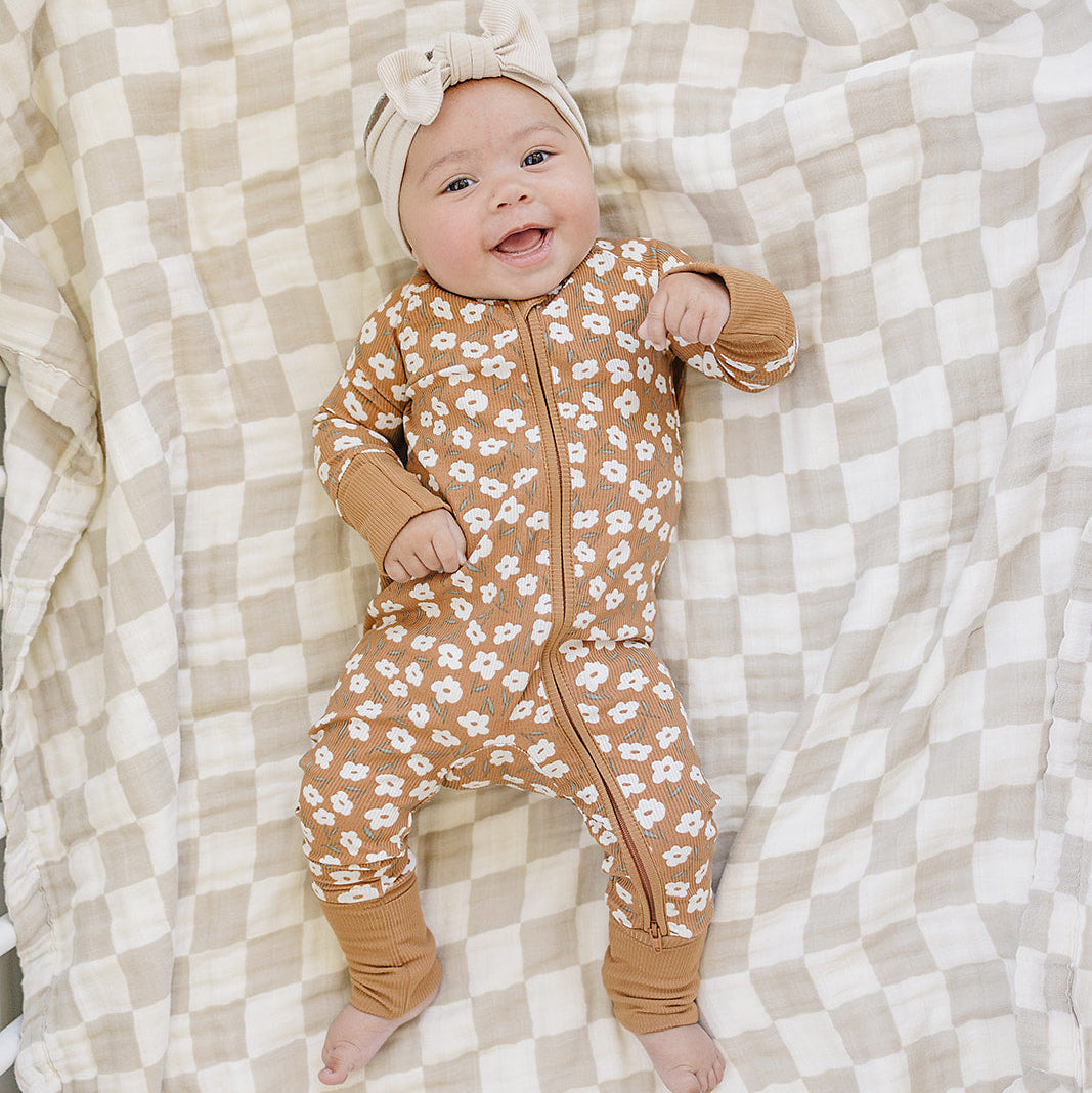 Baby in a floral onesie lying on a checkered blanket
