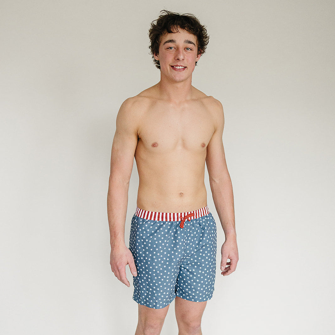 Man wearing blue patterned swim shorts with a white background