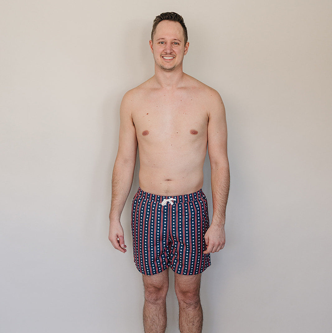 Man wearing patterned swim shorts against a plain background