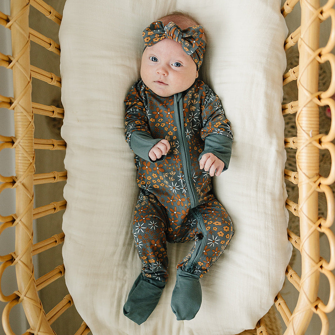 Baby in a patterned outfit lying on a white cushion inside a wicker crib.