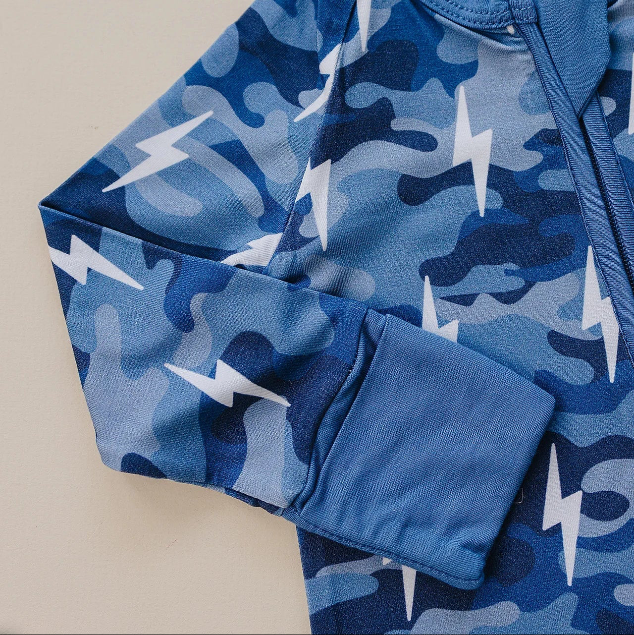 Blue camouflage long-sleeve shirt with lightning bolt pattern on a beige background