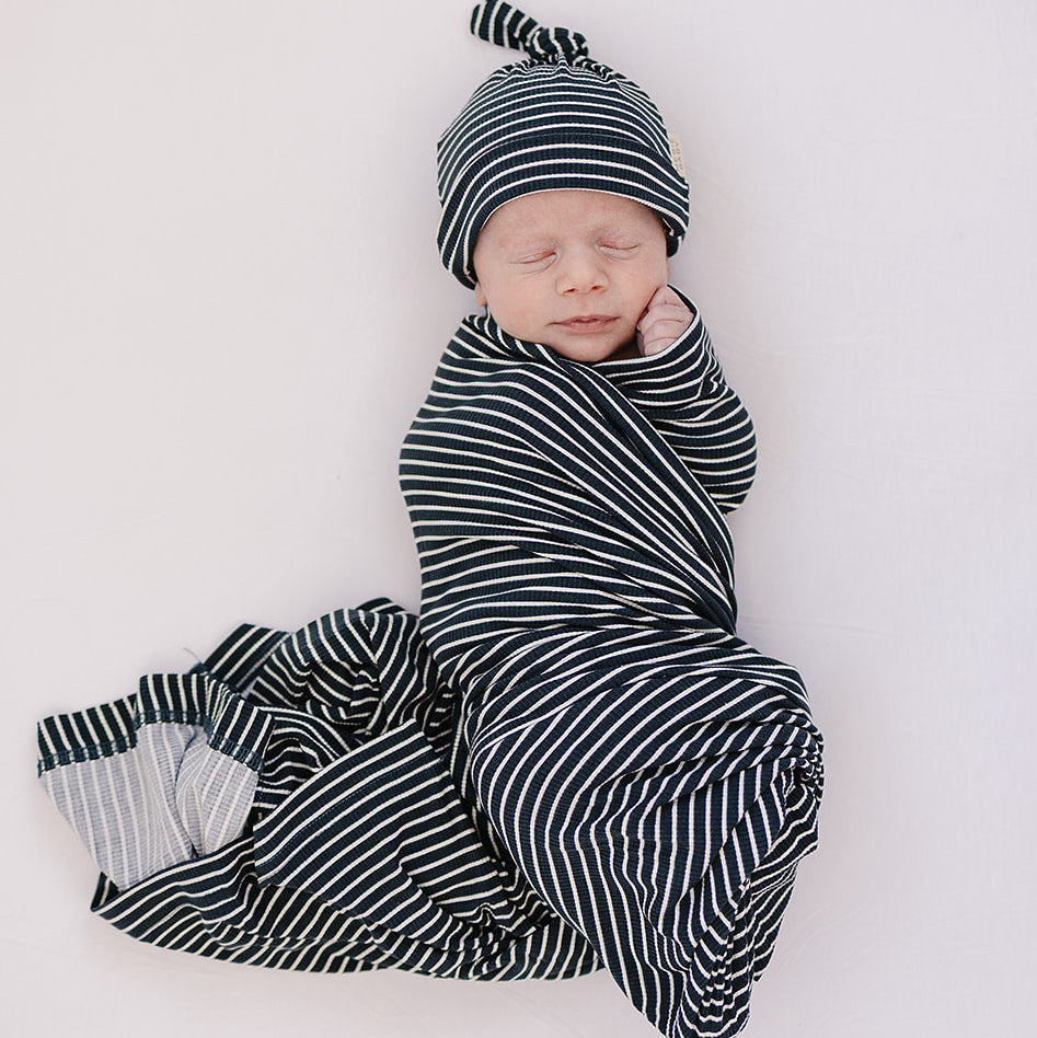 Newborn baby swaddled in a black and white striped outfit with matching hat on a white background