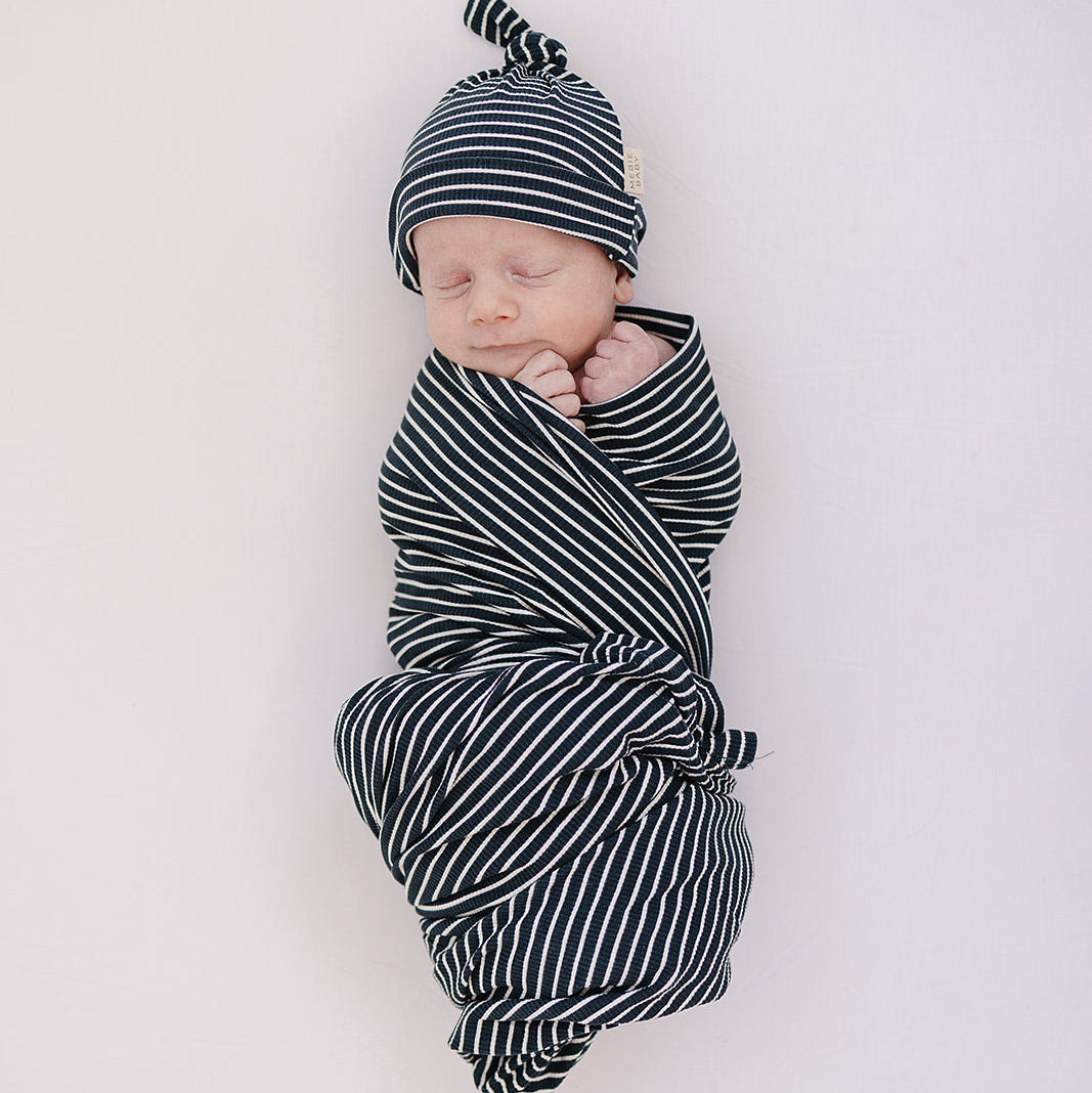 Newborn baby swaddled in black and white stripes on a light background