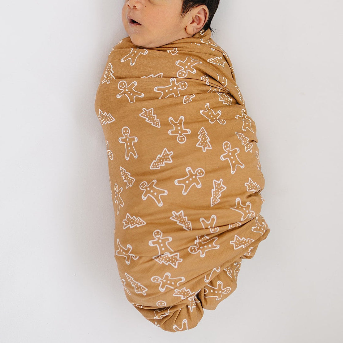 Baby wrapped in a brown blanket with white patterns on a white background