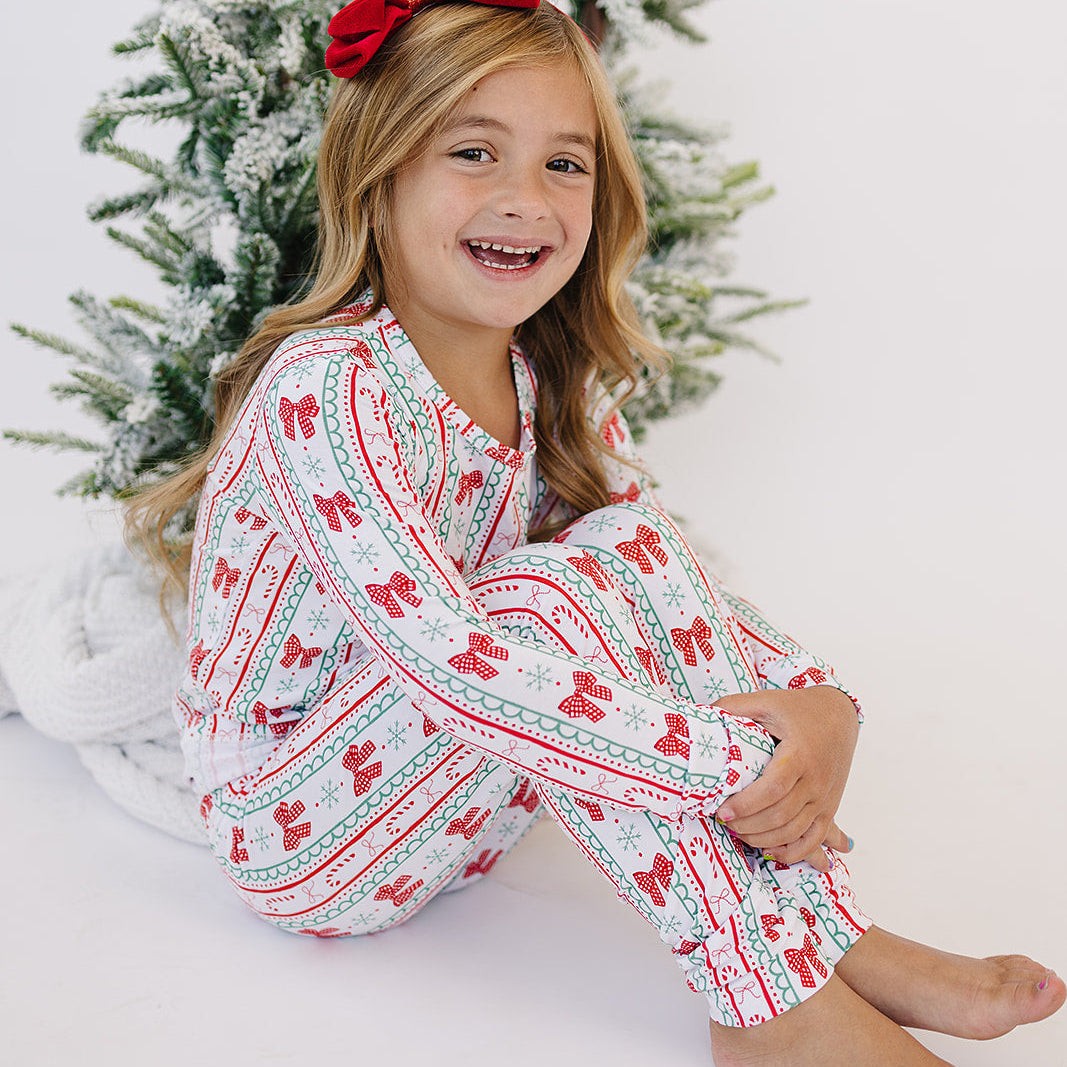 Young girl in festive pajamas sitting in front of a decorated Christmas tree.