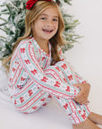 Young girl in festive pajamas sitting in front of a decorated Christmas tree.
