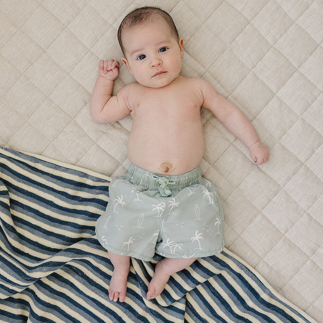 Baby lying on a quilted surface with a striped blanket