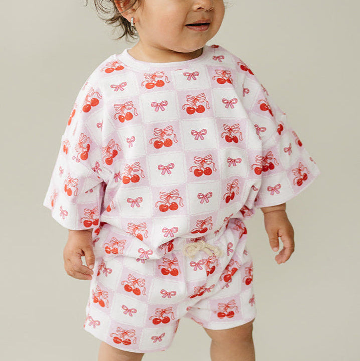 Baby wearing a white outfit with red cherry pattern on a neutral background