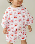 Baby wearing a white outfit with red cherry pattern on a neutral background