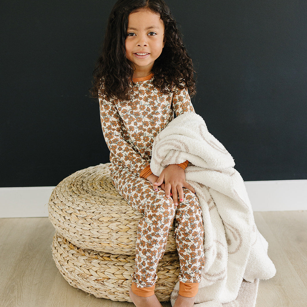 Child sitting on a woven ottoman with a blanket, wearing a patterned outfit against a black background.