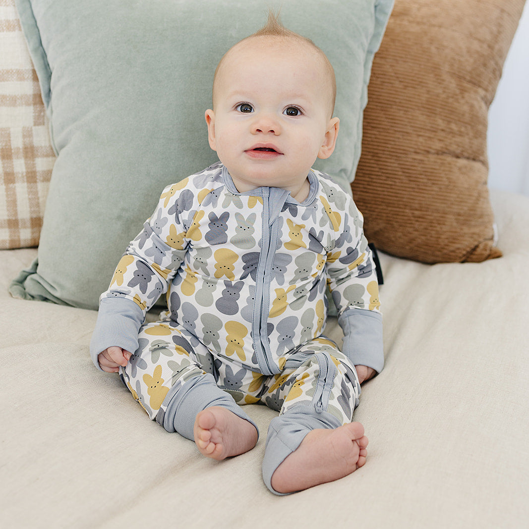 Baby in a patterned onesie sitting on a bed with pillows