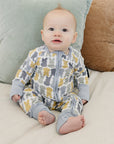 Baby in a patterned onesie sitting on a bed with pillows