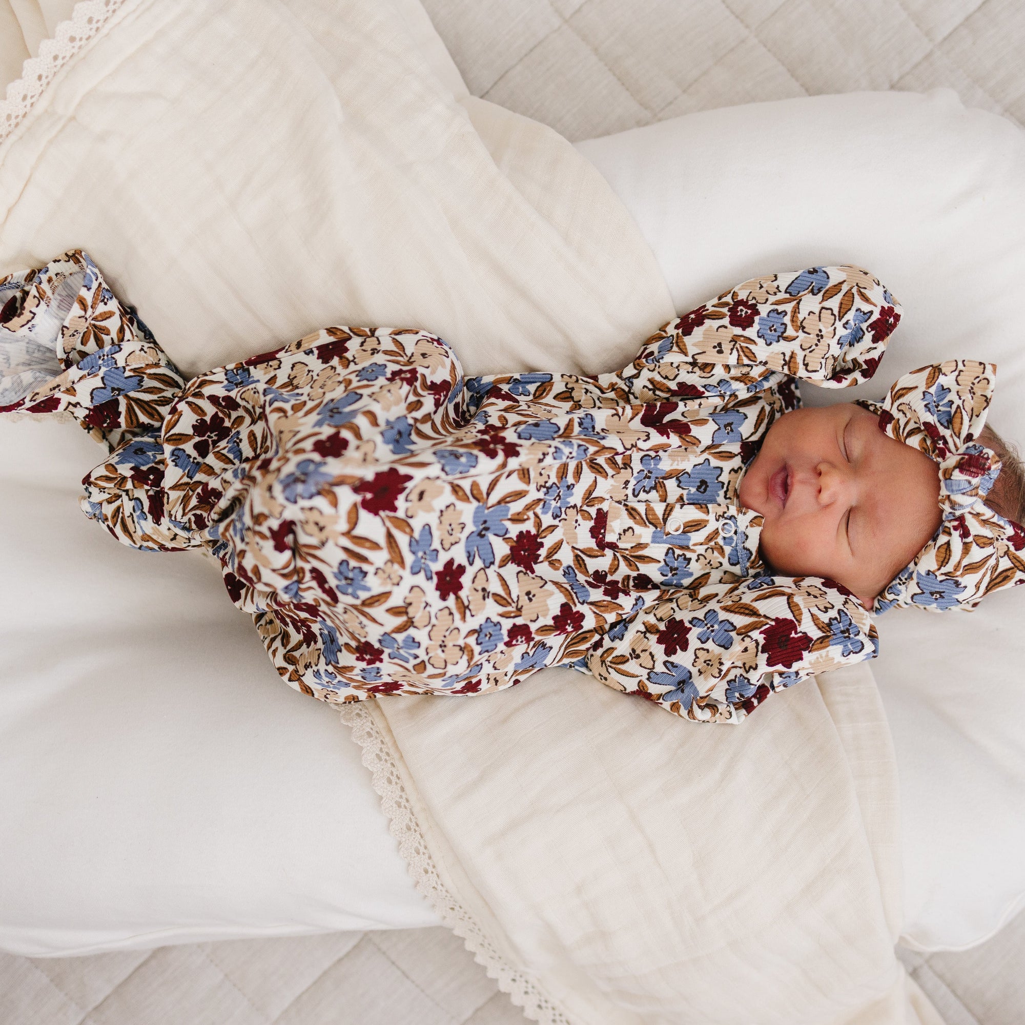 Newborn baby in a floral outfit lying on a white cushion