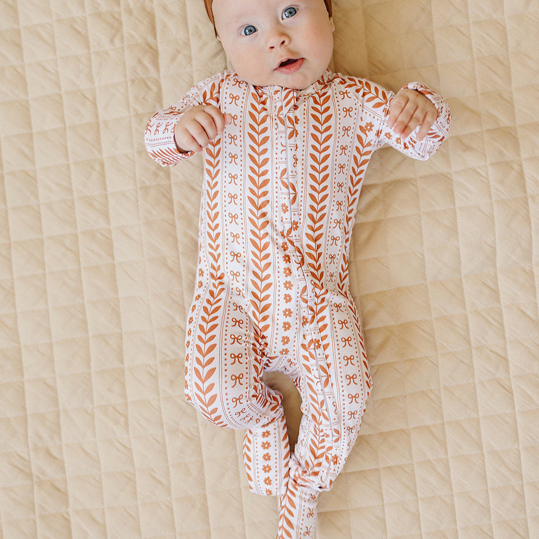 Baby wearing a patterned onesie and brown headband on a beige blanket