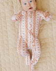 Baby wearing a patterned onesie and brown headband on a beige blanket