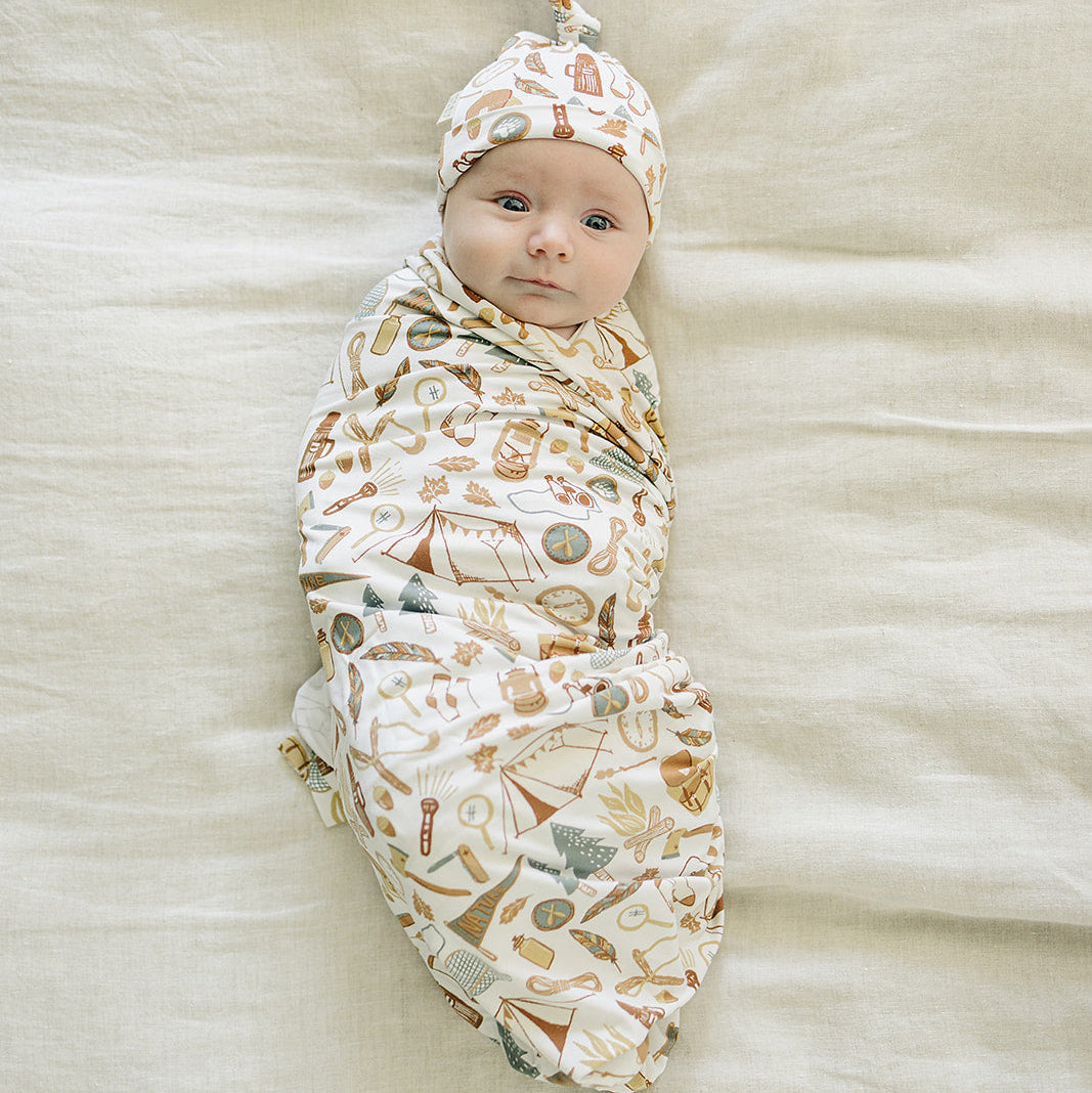 Newborn baby swaddled in a patterned blanket with a matching hat on a soft beige surface