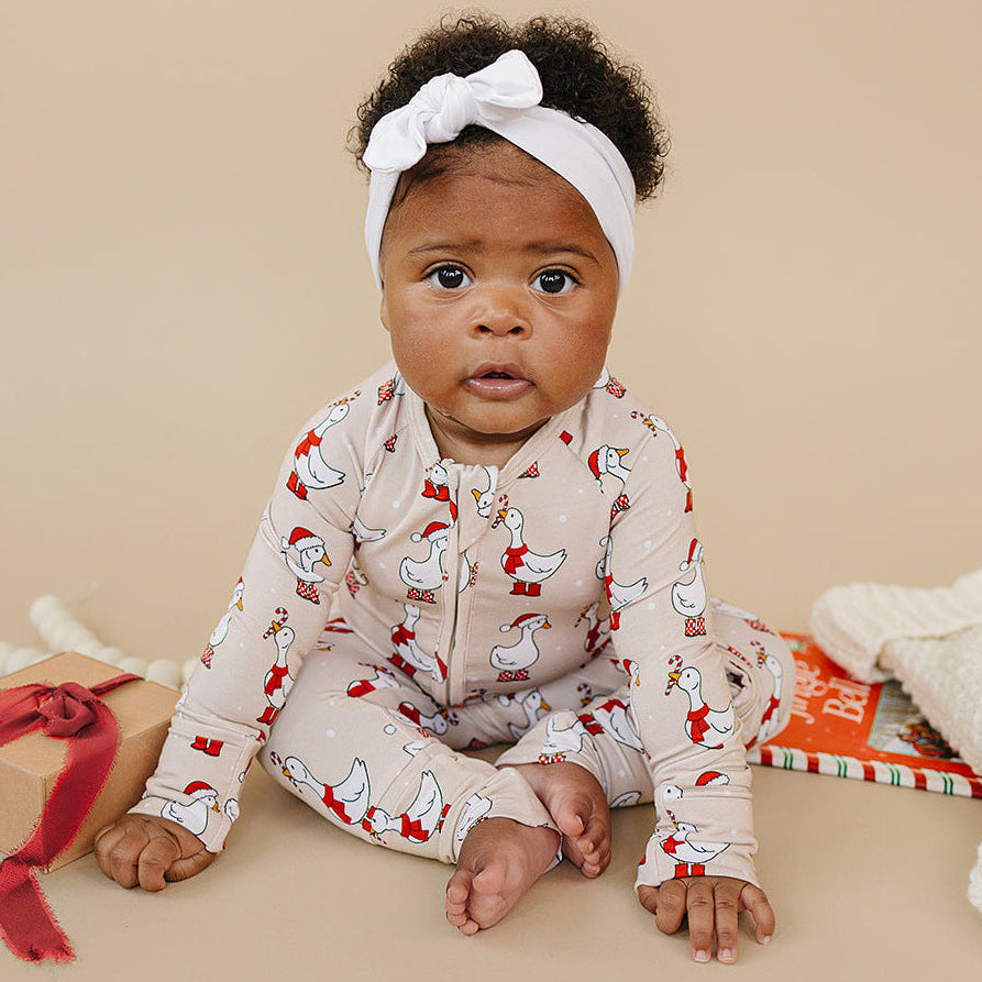 Baby wearing a patterned outfit with a white headband, sitting on a beige surface.