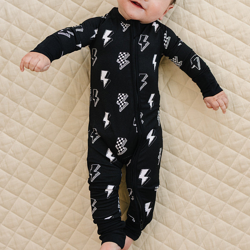 Baby wearing a black onesie with white patterns on a beige quilted surface
