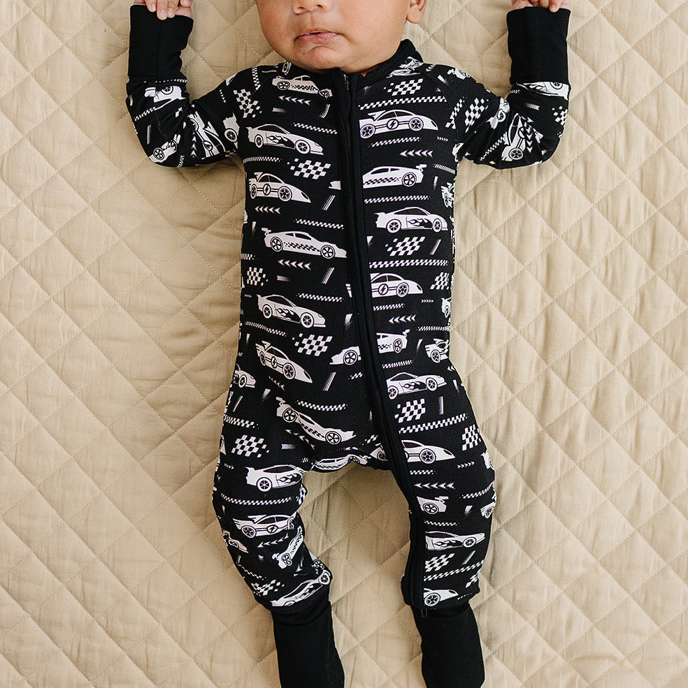 Baby wearing a black and white patterned onesie lying on a beige quilted surface.