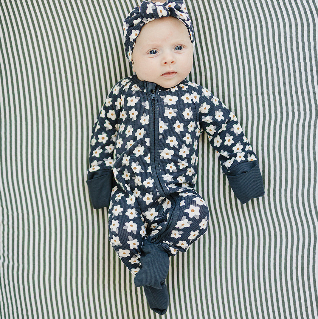 Baby in a floral onesie and headband lying on a striped fabric background