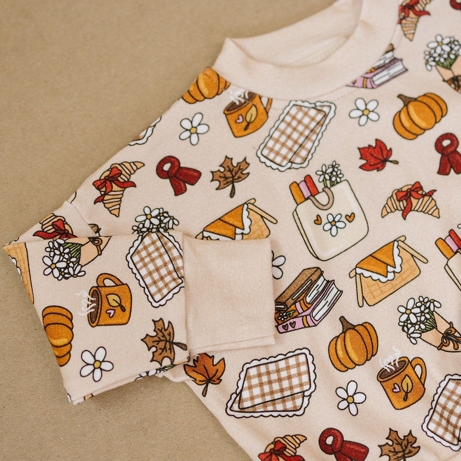 Fabric with autumn-themed pattern featuring pumpkins, leaves, and other fall elements on a beige background.