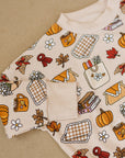 Fabric with autumn-themed pattern featuring pumpkins, leaves, and other fall elements on a beige background.