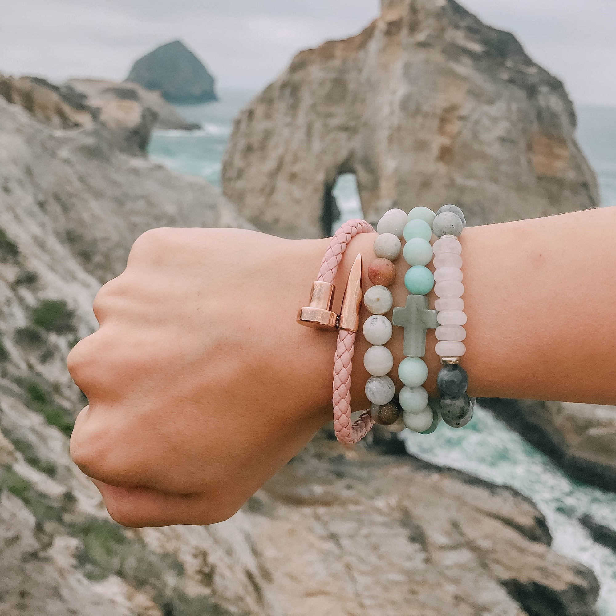 Person wearing multiple bracelets with a scenic background of rocks and water.