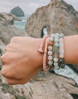 Person wearing multiple bracelets with a scenic background of rocks and water.