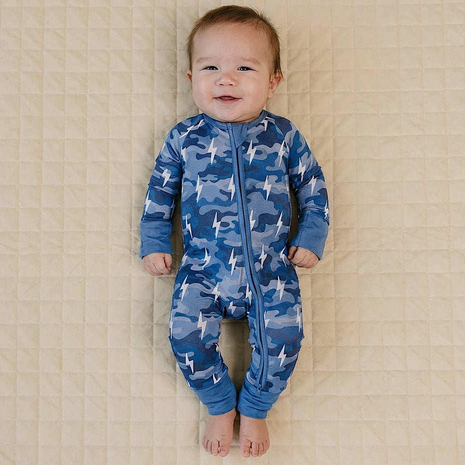 Baby wearing a blue shark print onesie lying on a beige quilted surface