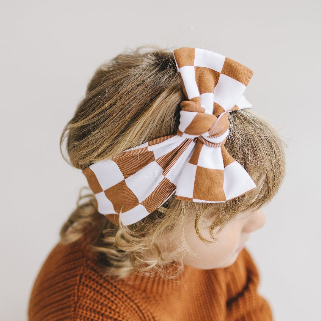 Child wearing a large checkered bow headband with a plain background