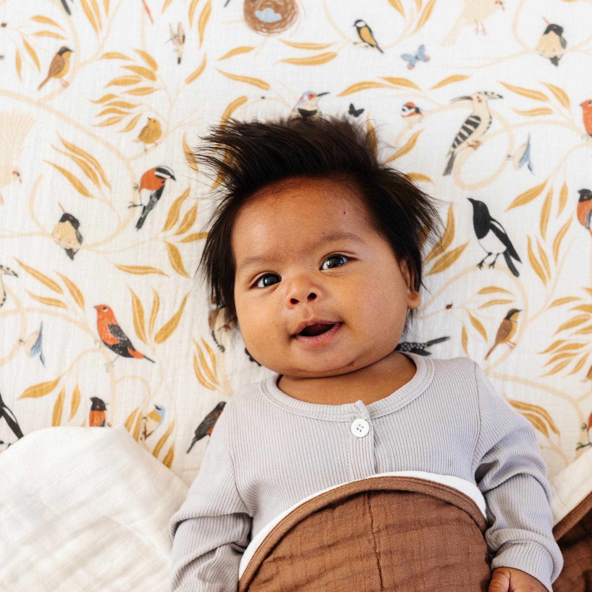 Baby in a crib with a patterned wall and brown blanket