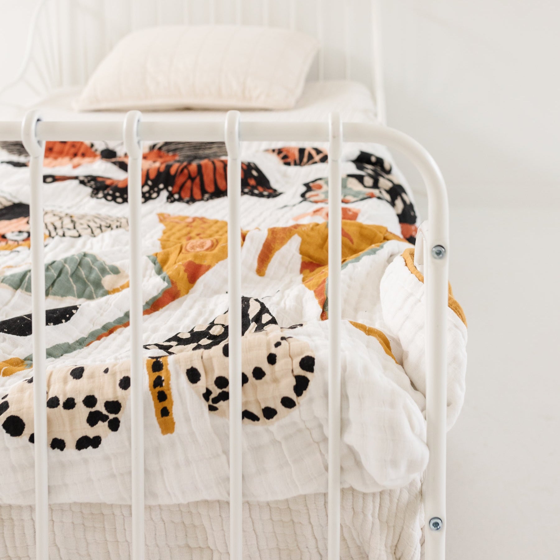 White metal bed with colorful bedding against a plain white wall
