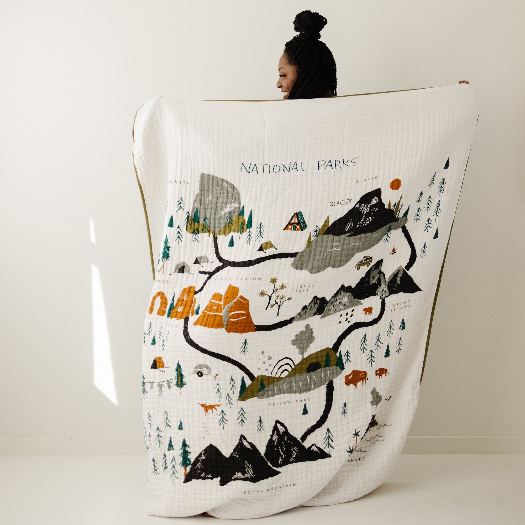 Person holding a large blanket with a map of national parks design on a plain background