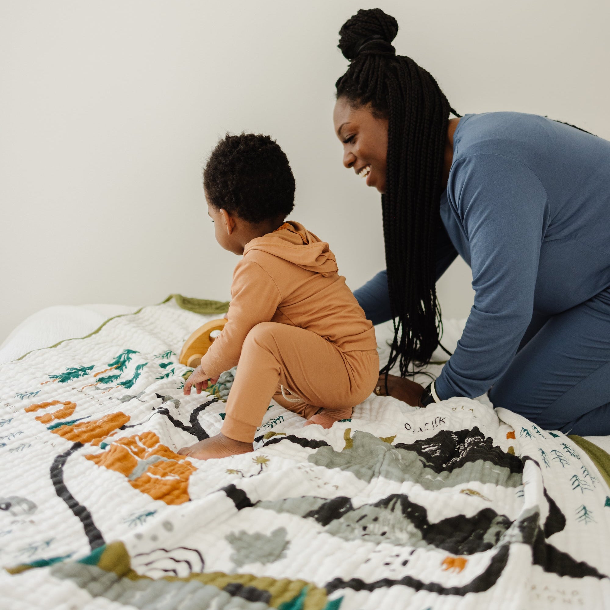 Woman and child playing on a colorful quilt against a white wall