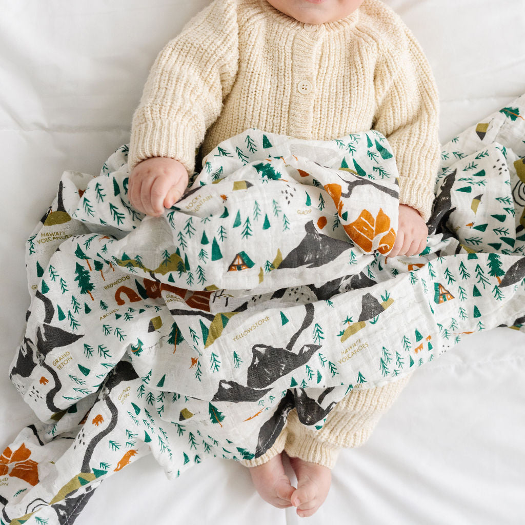Baby lying on a white blanket with a patterned blanket draped over them