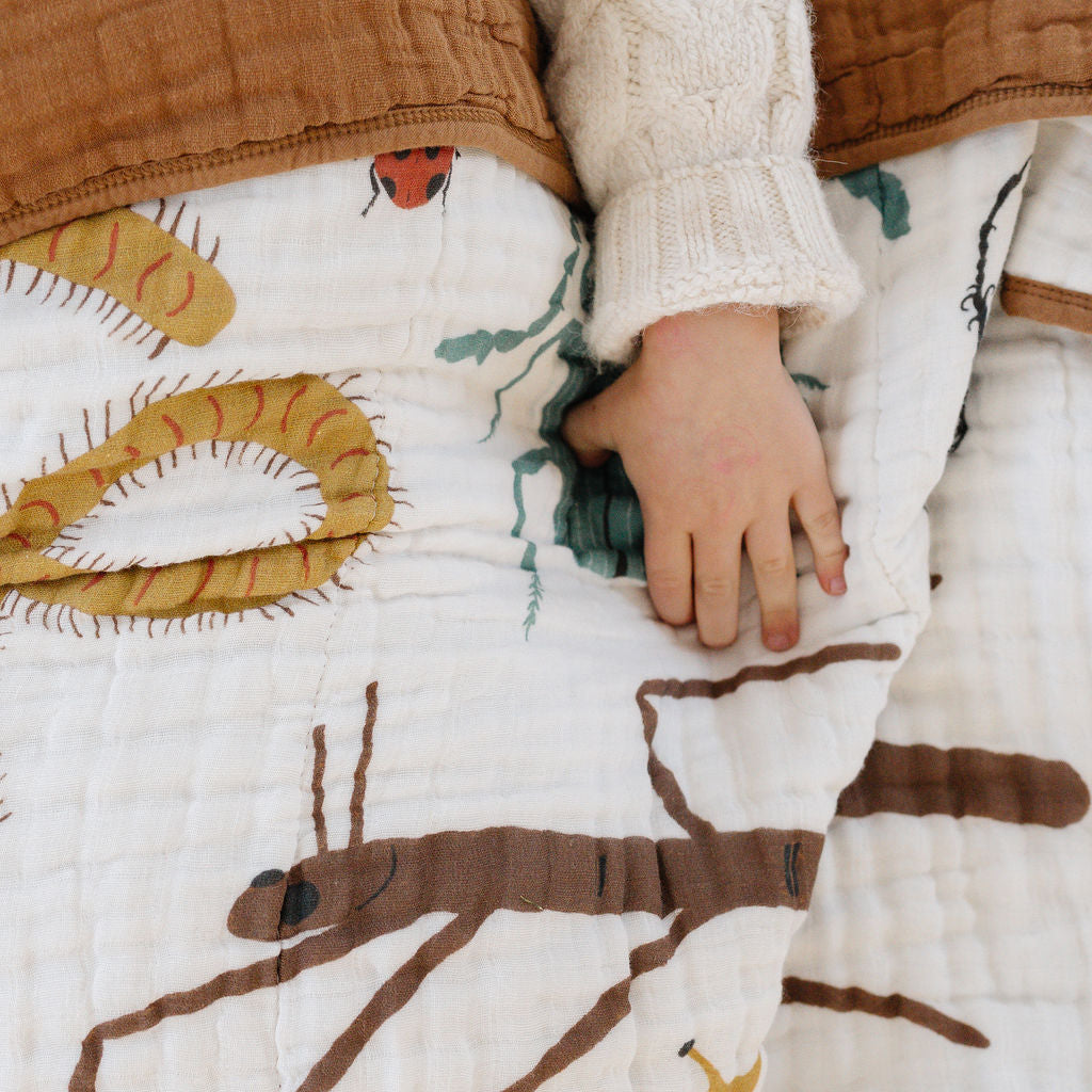 Person holding a quilt with dinosaur patterns, wearing a white sweater and brown pants.