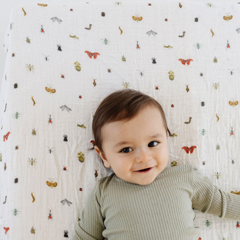 Baby in green ribbed outfit lying on a crib with a patterned sheet