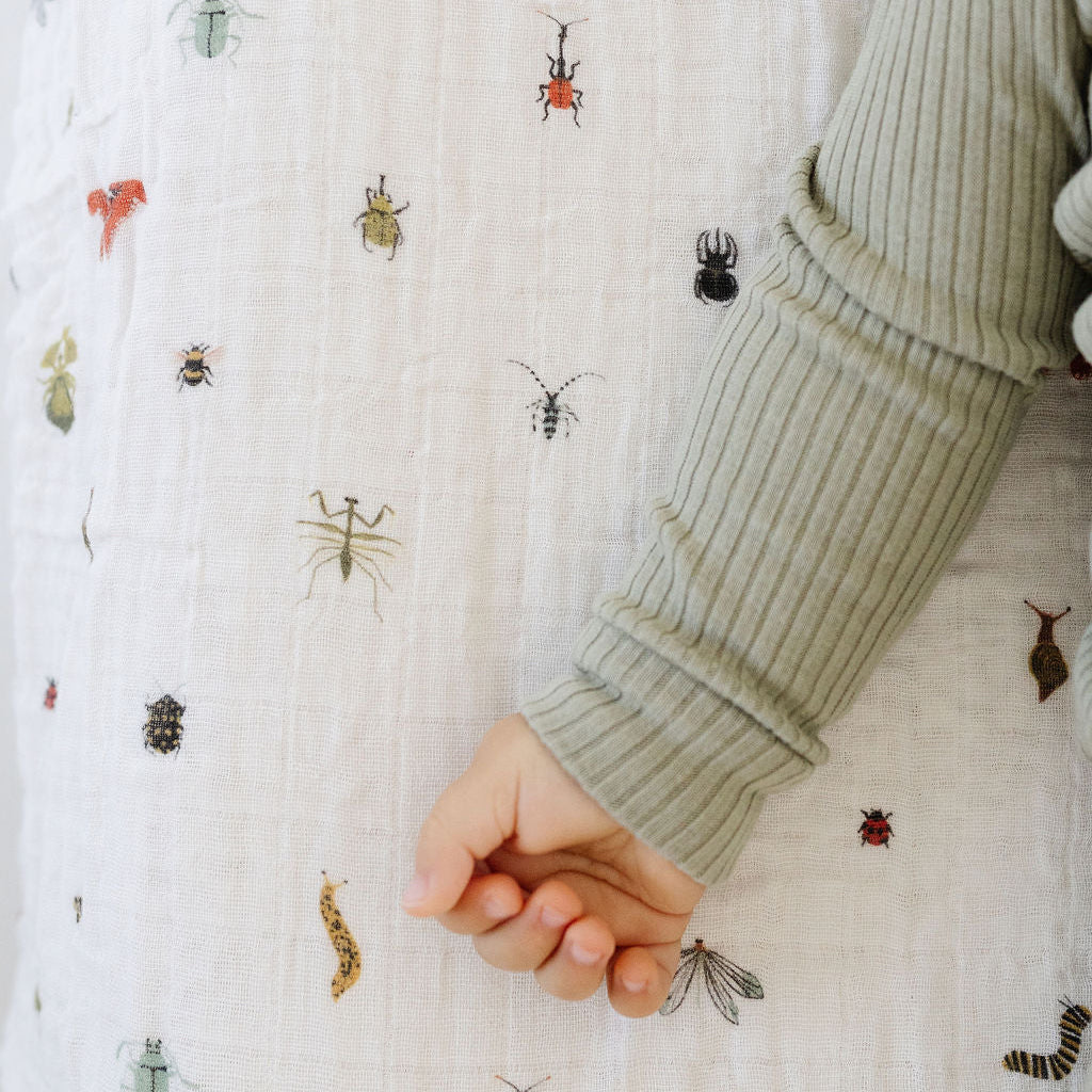 Close-up of a hand wearing a green sleeve against a white fabric background with insect patterns.