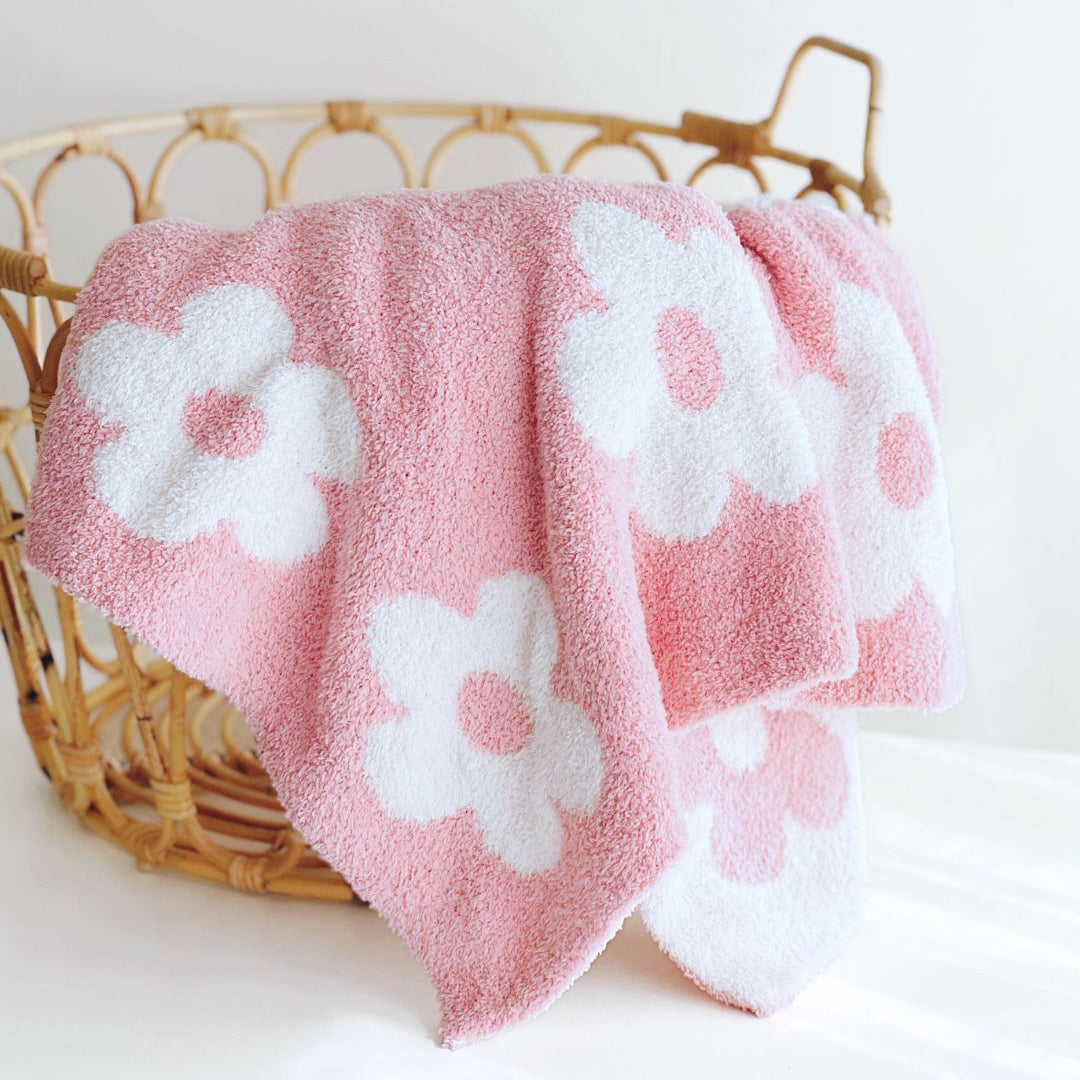 Pink towel with white floral patterns draped over a wicker basket on a white background