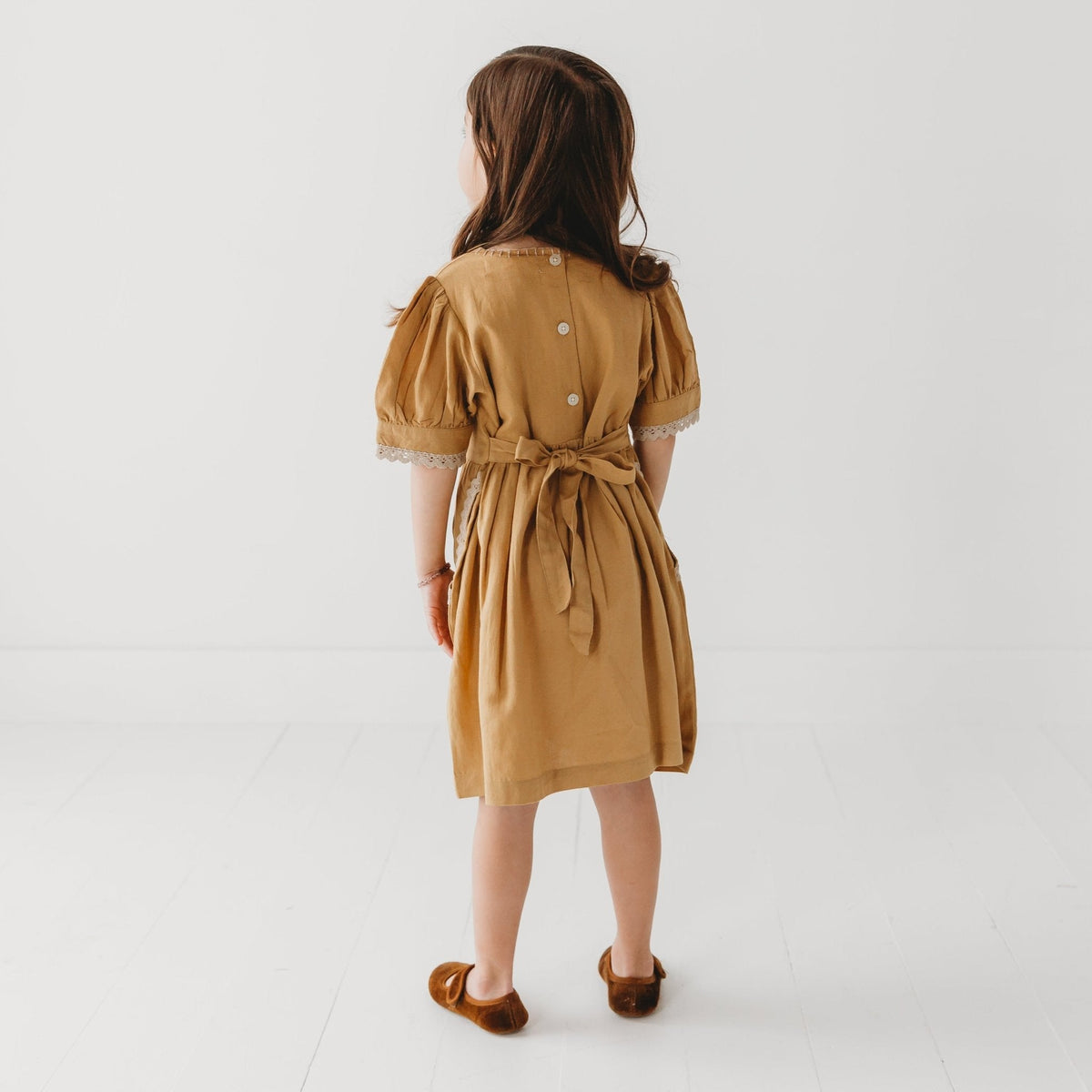 Back view of a girl wearing the mustard puff sleeve dress with a waist tie.