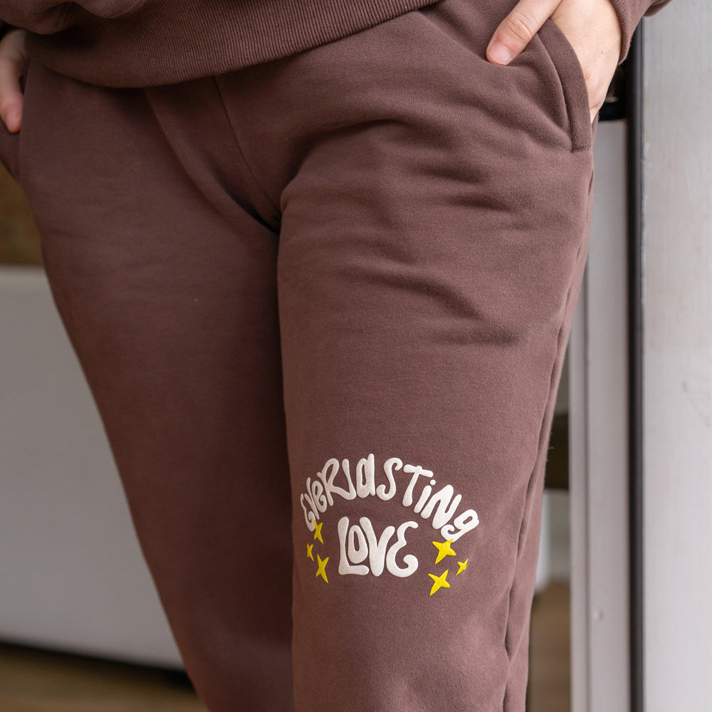 Brown sweatpants with 'Endless Love' text and stars on a blurred indoor background