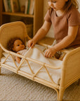 Child playing with a doll in a small bed in a cozy room with string lights and a bookshelf.