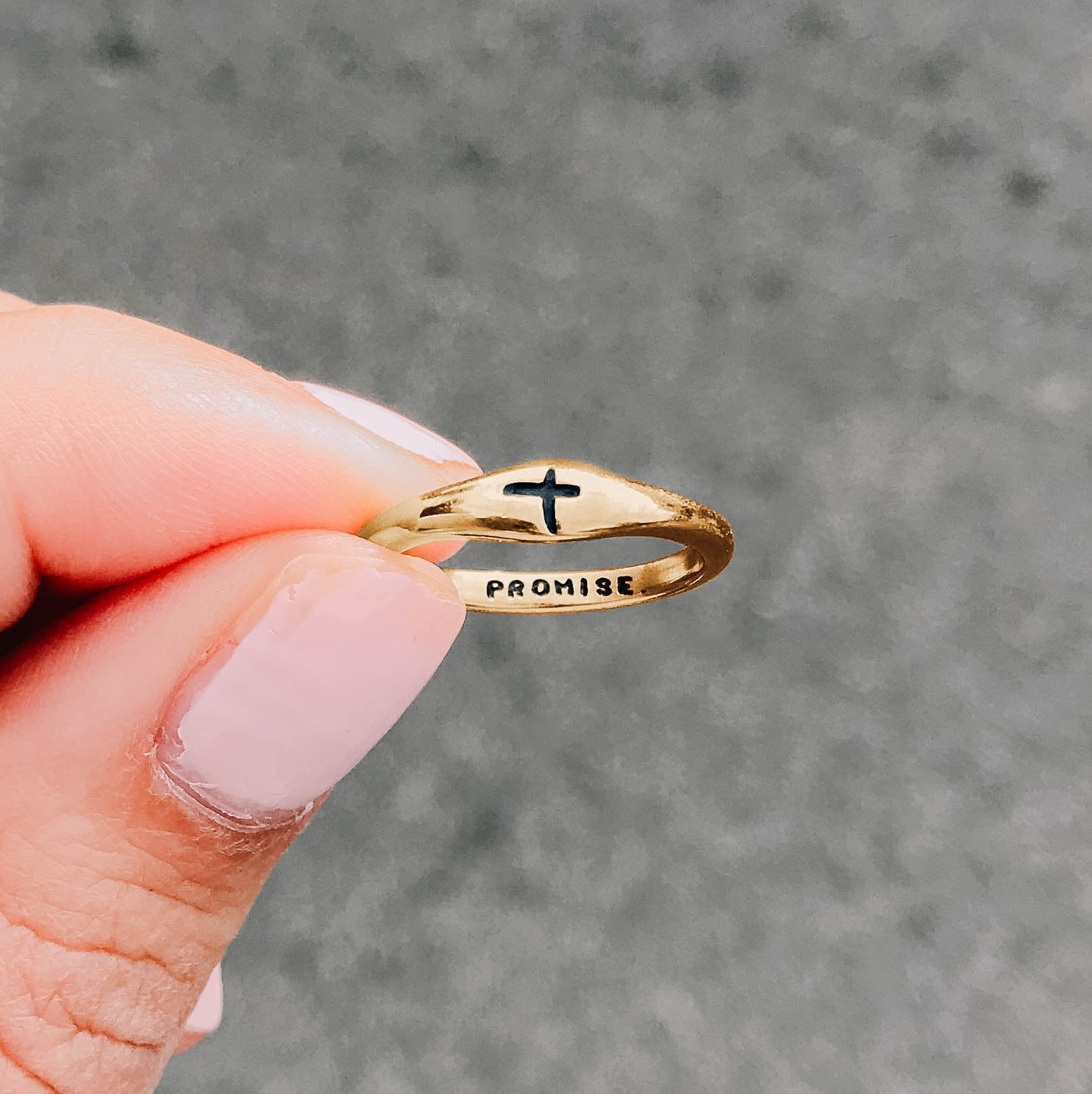 Gold ring with a cross design held by a hand against a gray background
