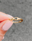 Gold ring with a cross design held by a hand against a gray background